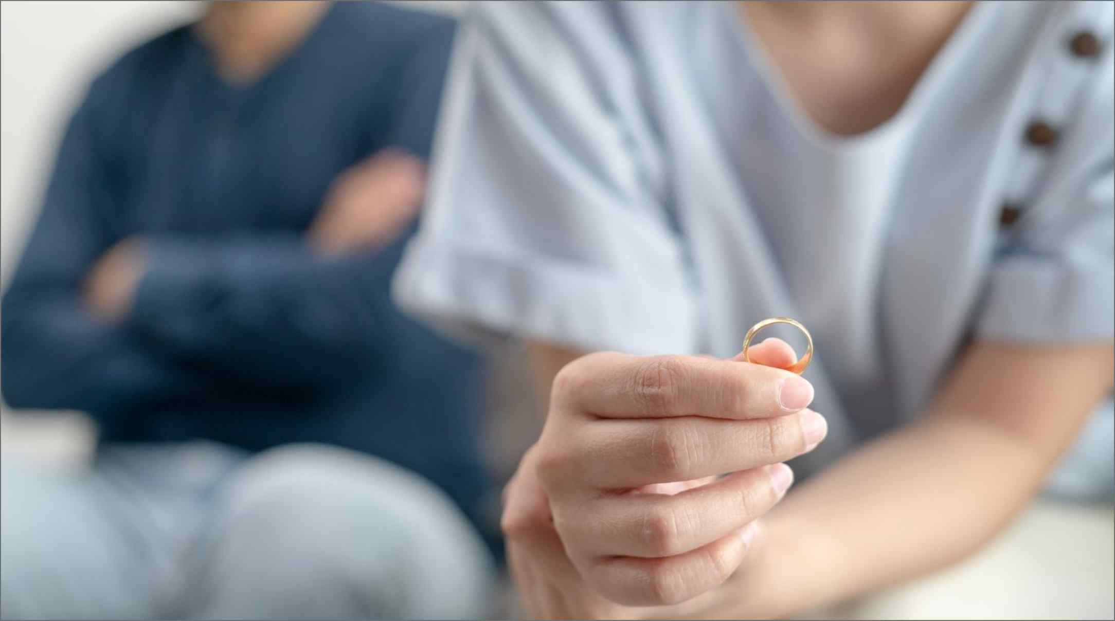 An unhappy couple sat with a woman holding up her wedding ring