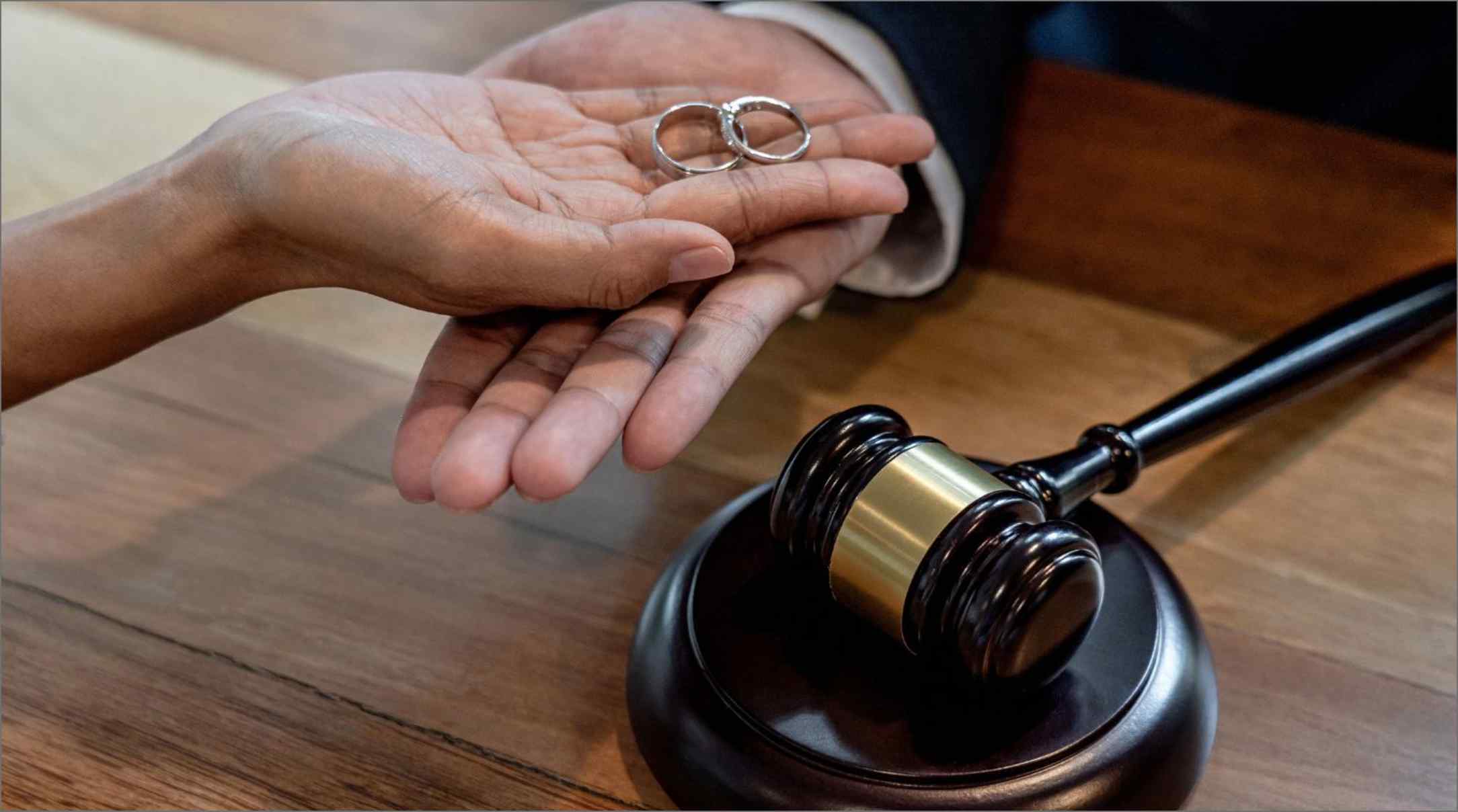 A person handing over wedding rings to a divorce lawyer with a black gavel on a wooden table